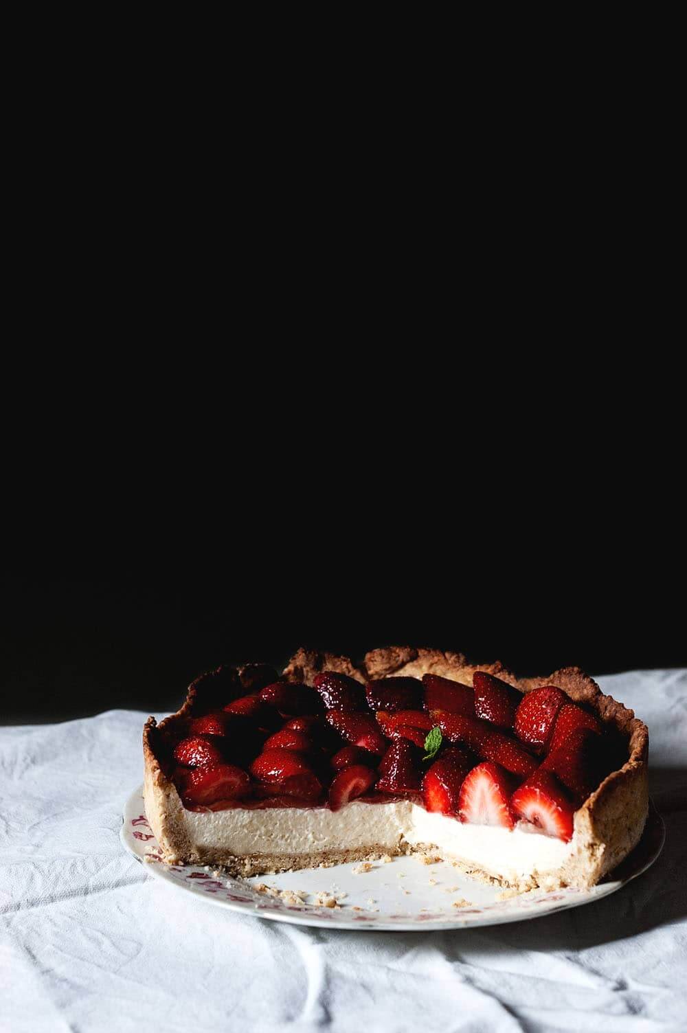 En una mesa cubierta con un mantel blanco está la tarta de fresas con crema y gelatina ya cortada.