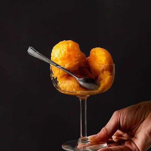 Una persona está sujetando en su mano una copa de helado. Dentro de la copa hay varias bolas de sorbete de mandarina sin alcohol.
