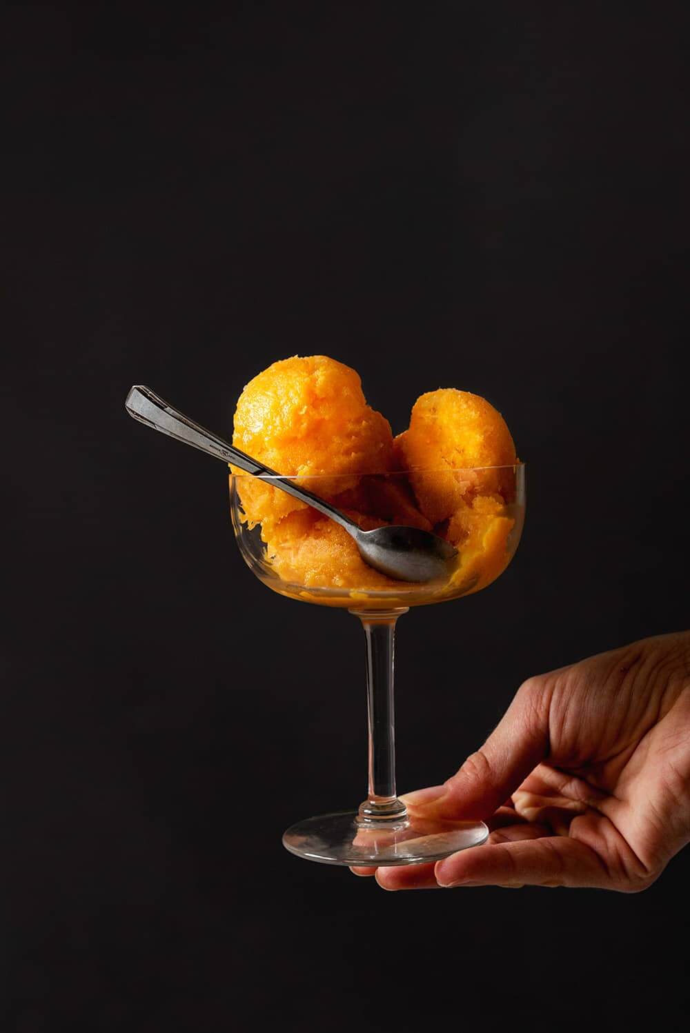 Una persona está sujetando en su mano una copa de helado. Dentro de la copa hay varias bolas de sorbete de mandarina sin alcohol.