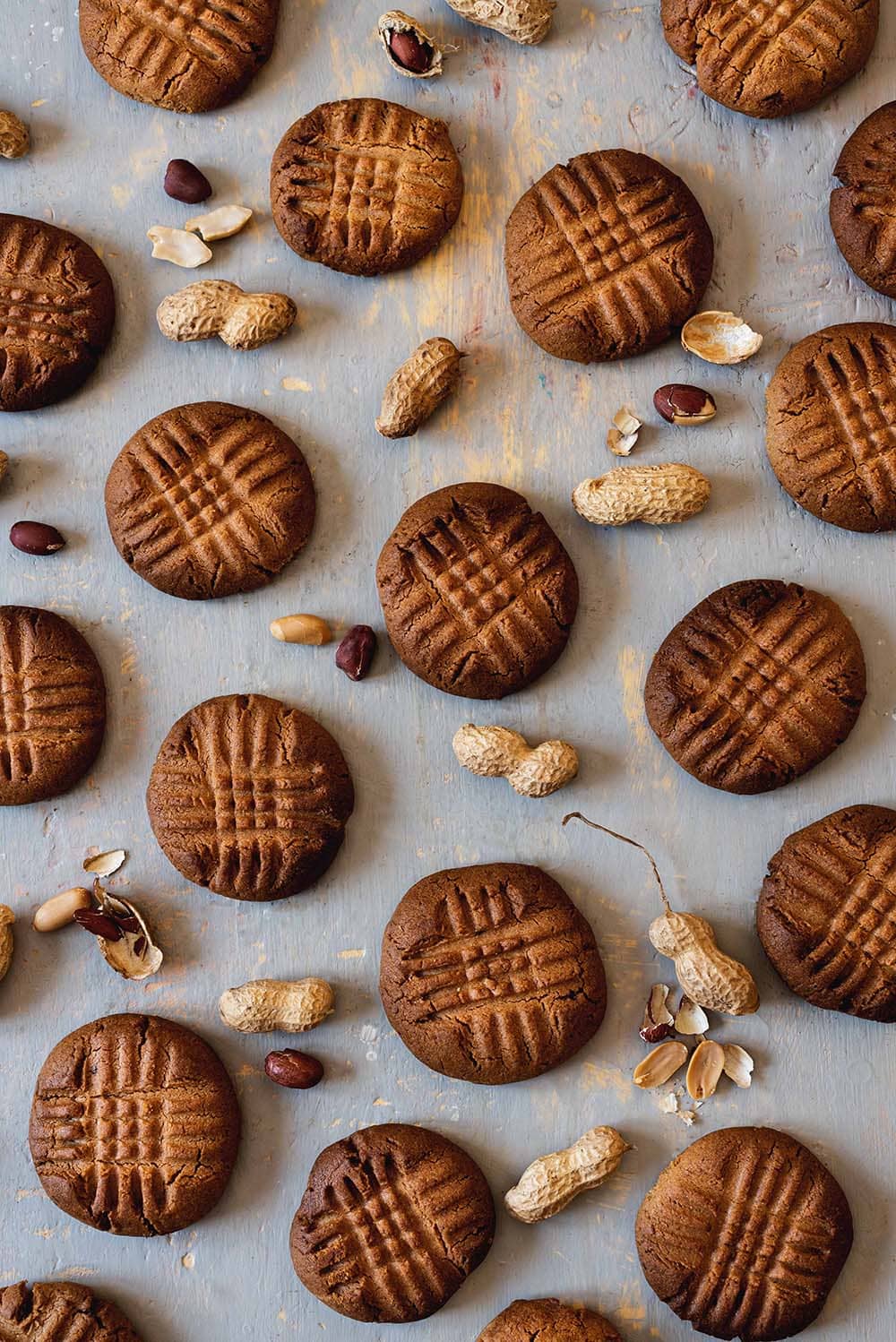 En una superficie gris están puestas las galletas de mantequilla de cacahuete crujientes junto con unos cacahuetes en sus cáscaras.