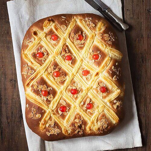 En una mesa de madera está puesto un paño de cocina. Encima está puesta la Coca de San Juan con crema pastelera. Al lado hay un cuchillo.