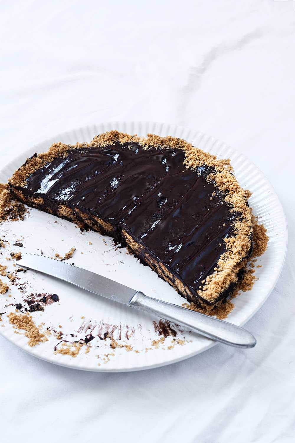 En una mesa cubierta con mantel blanco hay un plato blanco. Encima está la tarta de chocolate con galleta ya cortada. Al lado del postre hay un cuchillo.