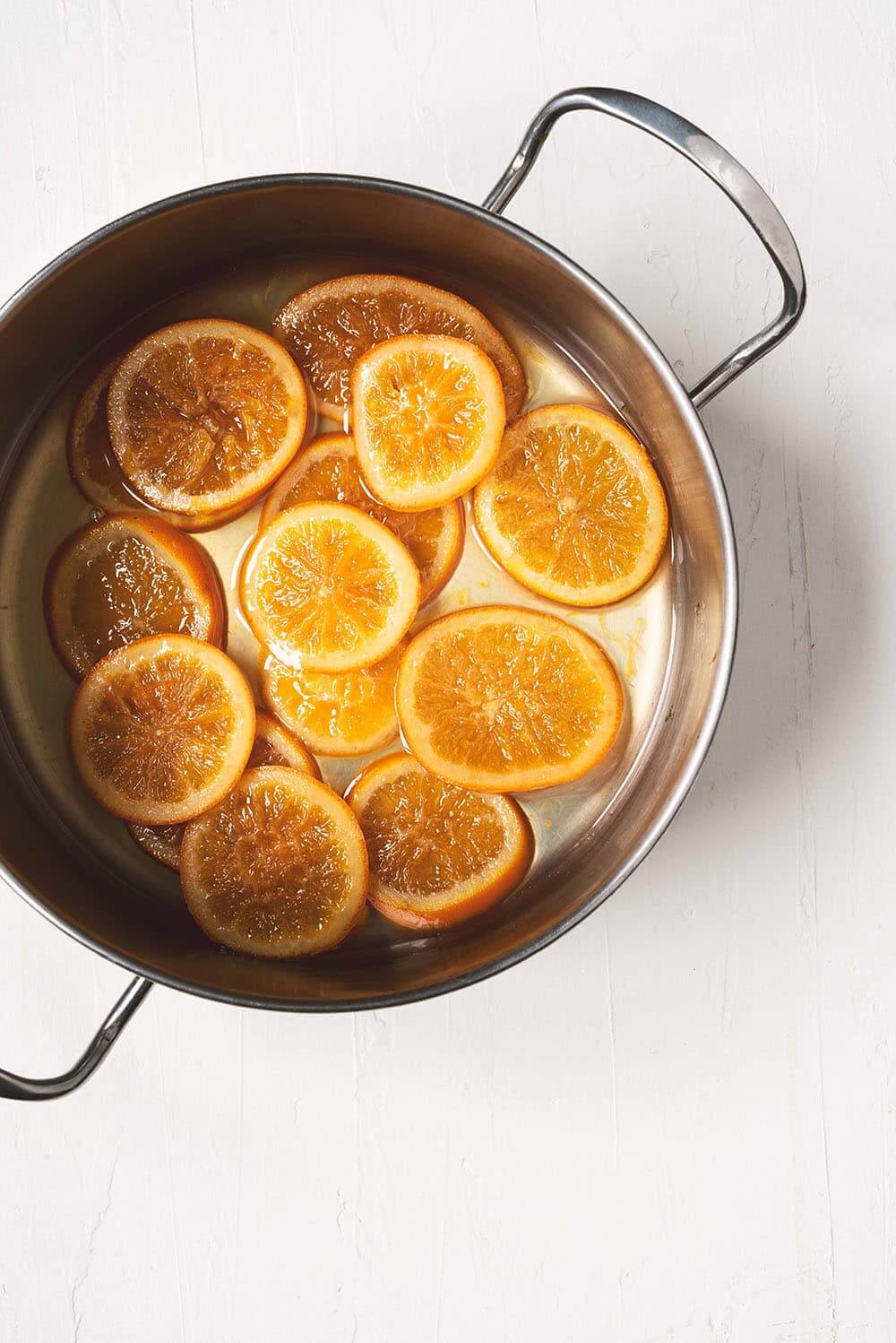 En una mesa blanca está una cazuela con muchas rodajas de naranja confitada casera.