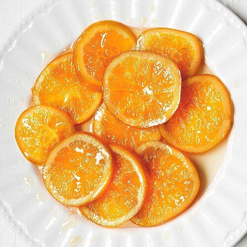 En una mesa blanca está un plato blanco con muchas rodajas de naranja confitada casera.