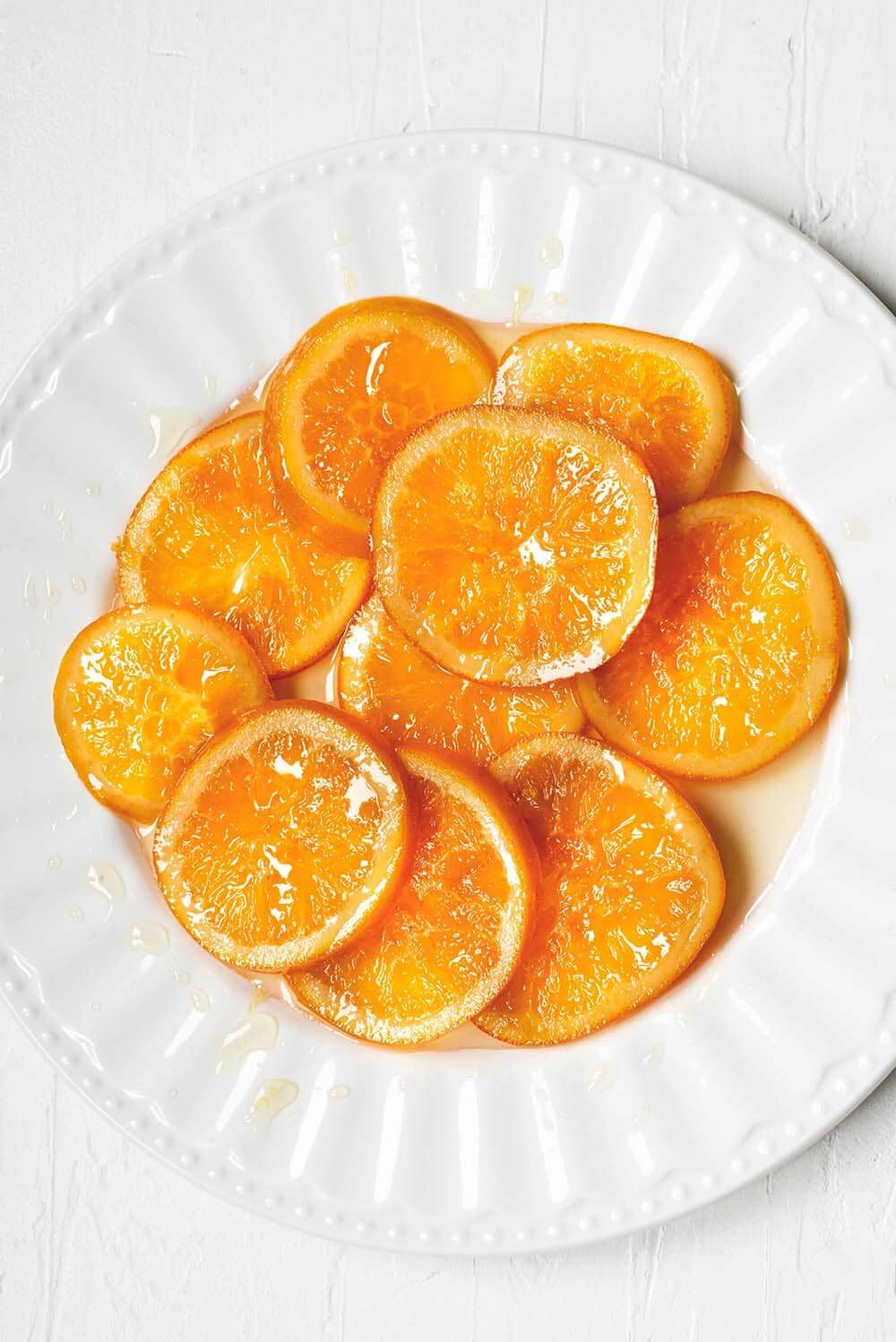 En una mesa blanca está un plato blanco con muchas rodajas de naranja confitada casera.