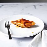 En una mesa de mármol está un plato blanco. En el plato hay pestiños crujientes con miel. Al lado del postre hay un tenedor.