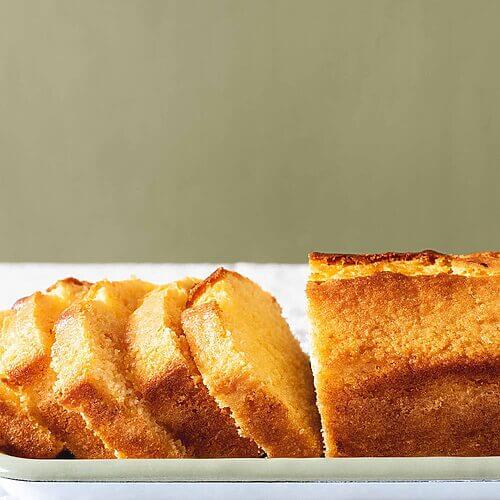 En una mesa hay un mantel blanco. En la mesa hay una bandeja blanca. En esta bandeja están las rodajas de Madeira cake cortadas.