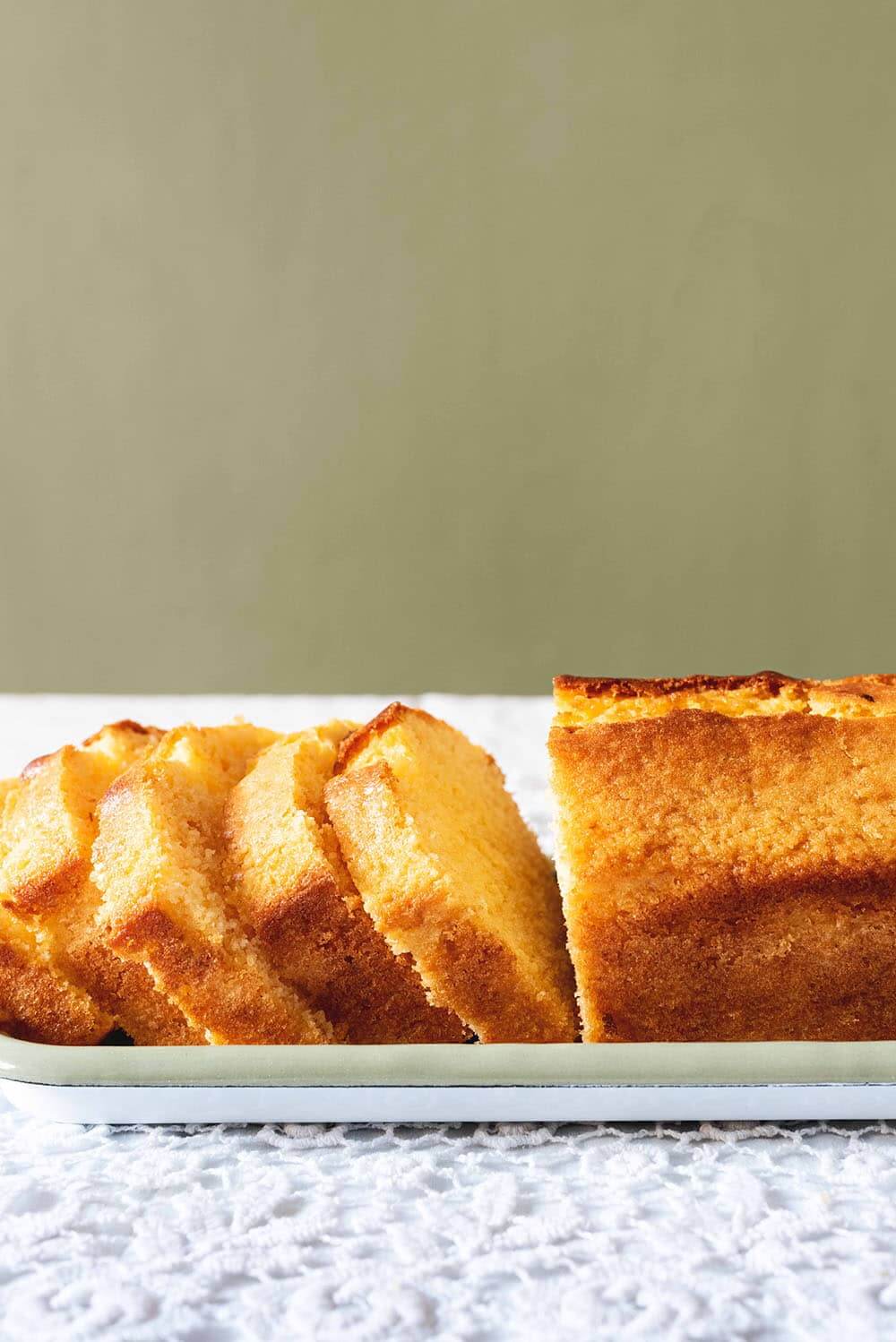 En una mesa hay un mantel blanco. En la mesa hay una bandeja blanca. En esta bandeja están las rodajas de Madeira cake cortadas.