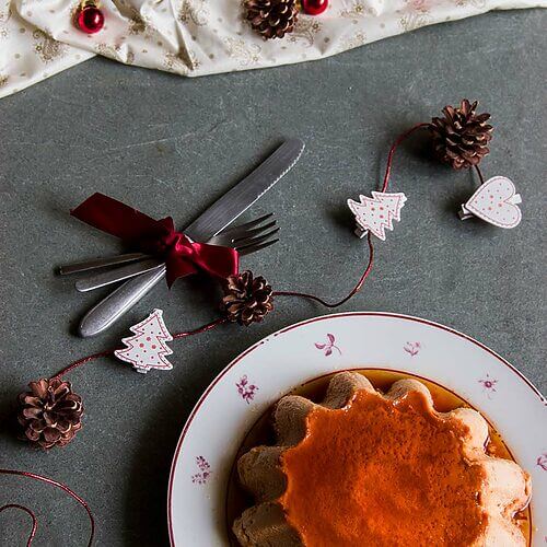 En una mesa de piedra hay un plato. En el medio está el flan de turrón de Jijona. Alrededor hay decoraciones navideñas.