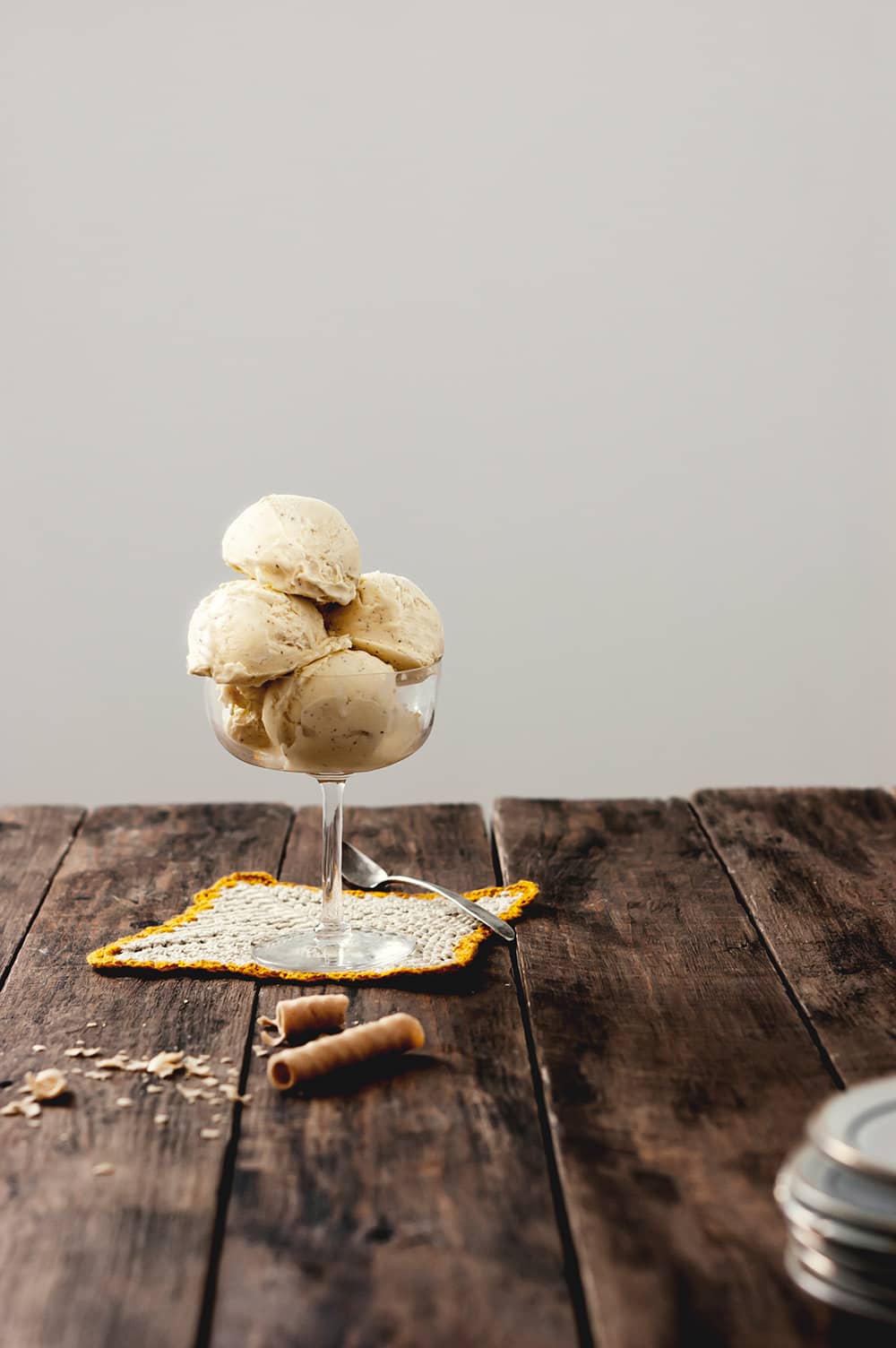 En una mesa de madera hay una copa llena de helado casero de vainilla sin máquina. Alrededor hay galletas desmigadas.