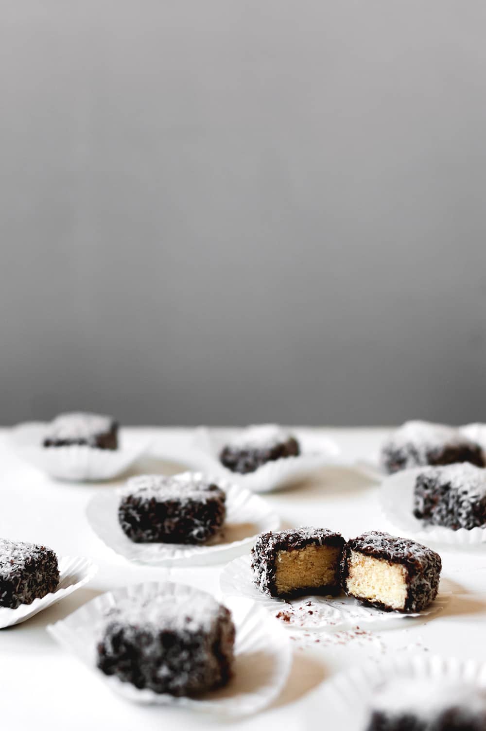 En una mesa de madera blanca hay varios Lamingtons, un postre australiano.