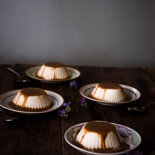 En una mesa de madera hay varios platos pequeños. En cada una hay panna cotta con salsa de toffe.