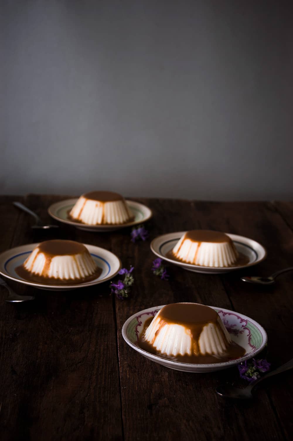 En una mesa de madera hay varios platos pequeños. En cada una hay panna cotta con salsa de toffe.