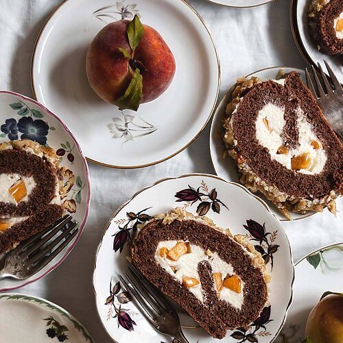 Una mesa cubierta con mantel blanco hay varios platos. En cada una hay una rodaja de brazo de gitano de nueces relleno con crema de chocolate blanco.