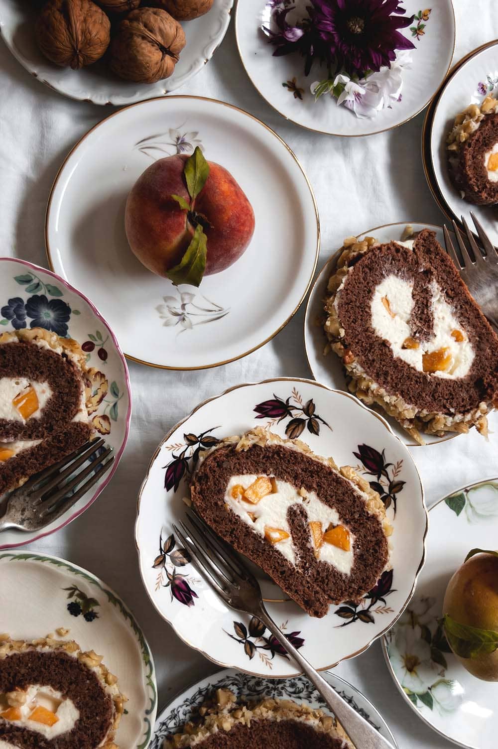 Una mesa cubierta con mantel blanco hay varios platos. En cada una hay una rodaja de brazo de gitano de nueces relleno con crema de chocolate blanco.