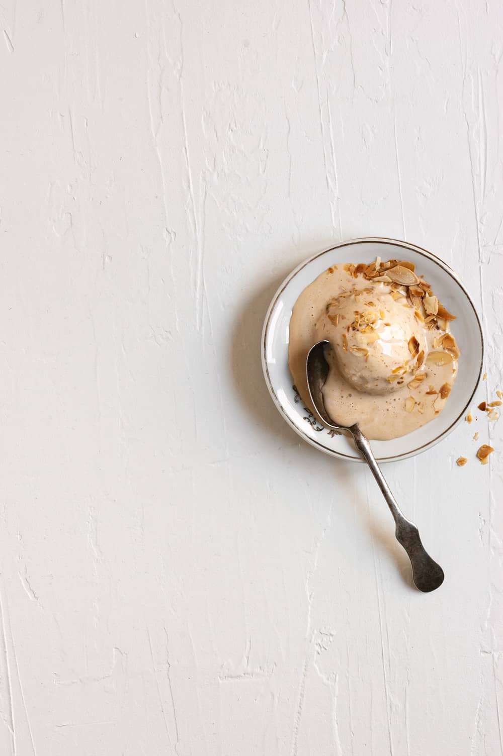 En una mesa de madera blanca hay un plato. En él hay una bola de helado de turrón sin heladera. Al lado del plato hay una cuchara.