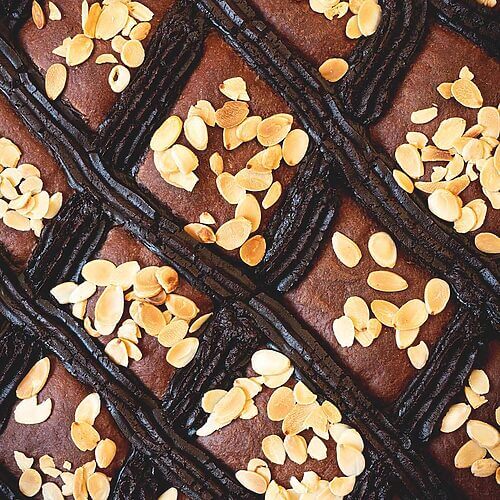 Se ve muy cerca la coca de San Juan. Se ven las almendras fileteadas tostadas, y la tiras de crema pastelera de chocolate.