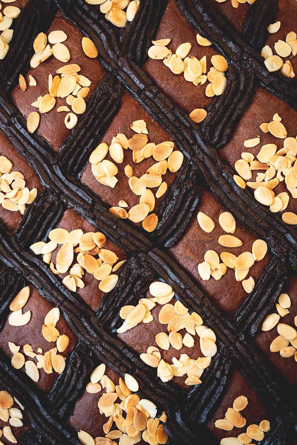 Se ve muy cerca la coca de San Juan. Se ven las almendras fileteadas tostadas, y la tiras de crema pastelera de chocolate.