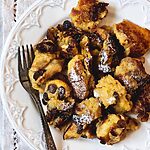 Una mesa está cubierta con un paño blanco. Encima hay un plato blanco vintage. En el plato hay una reacción de Kaiserschmarrn. En el plato hay un tenedor.