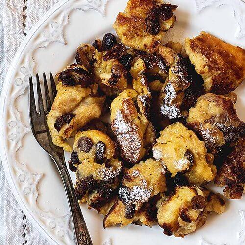Una mesa está cubierta con un paño blanco. Encima hay un plato blanco vintage. En el plato hay una reacción de Kaiserschmarrn. En el plato hay un tenedor.