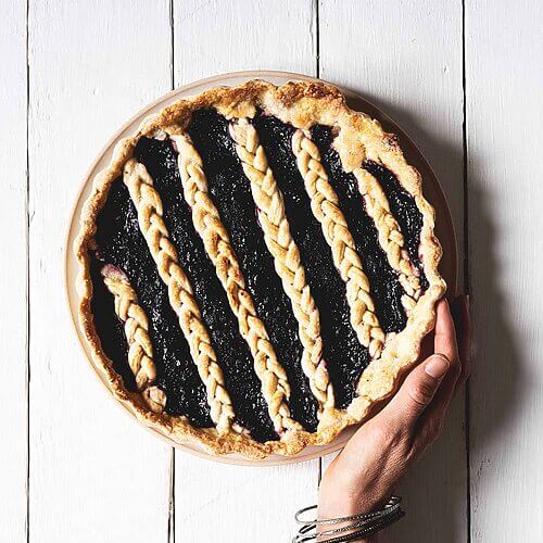 En una mesa blanca está puesto el Pie de frutos rojos. Una mano está tocando la tarta.