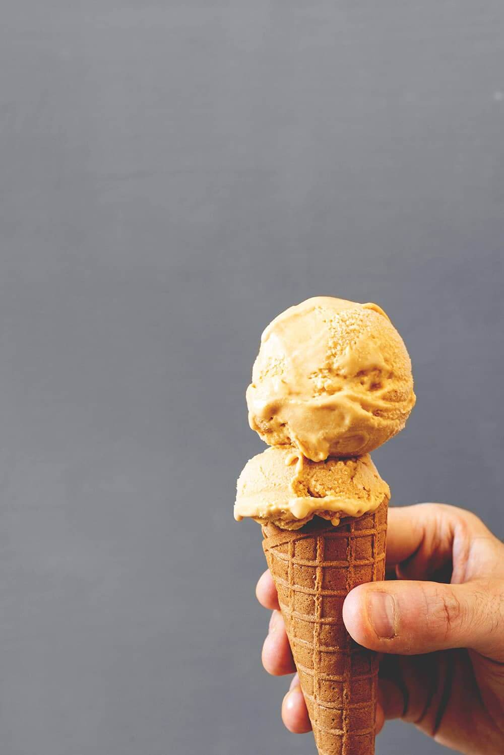 Una persona está sujetando en la mano un cucurucho. En el cucurucho hay dos bolas de helado de caramelo salado cremoso.