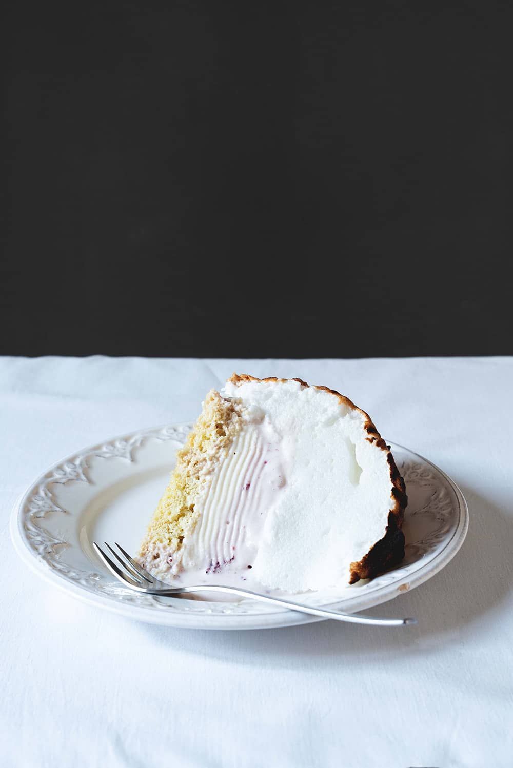 Soufflé Alaska Una mesa está cubierta con un mantel blanco. Encima hay un plato blanco con un trozo de Soufflé Alaska. Está volcado.