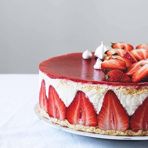 En una mesa cubierta con un mantel blanco. Encima está un plato blanco. Se ve desde cerca la bonita decoración de la Tarta Fraisier.