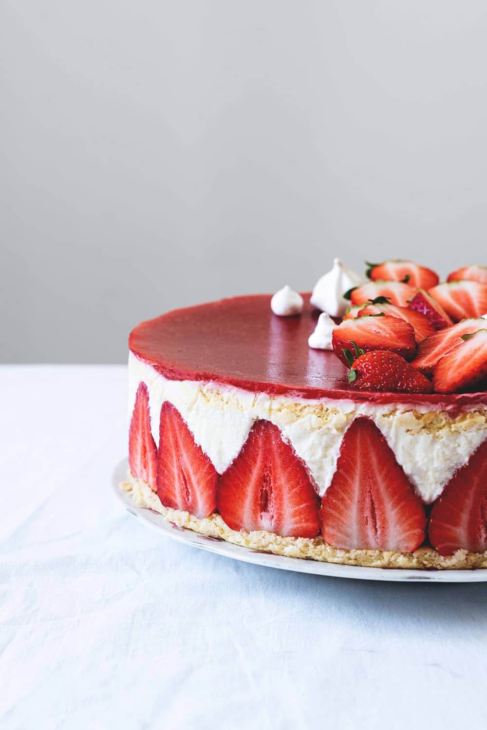 Tarta Fraisier receta francesa En una mesa cubierta con un mantel blanco. Encima está un plato blanco. Se ve desde cerca la bonita decoración de la Tarta Fraisier.