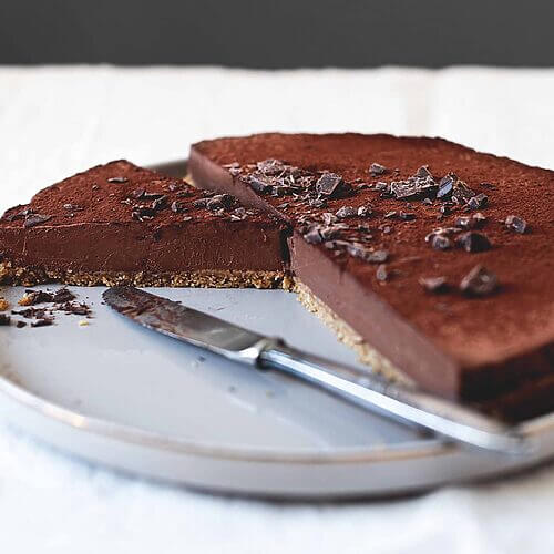 En una mesa gris está un plato gris. Encima está la tarta de queso de chocolate sin horno. Ya está cortado. Se ve muy cremosa.