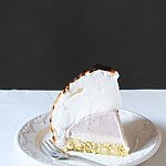 Una mesa está cubierta con un mantel blanco. Encima hay un plato blanco con un trozo de Tortilla noruega. Está de pie.