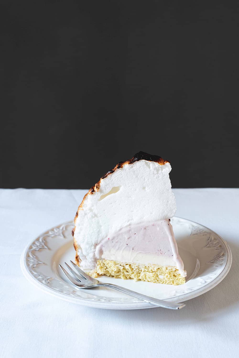 Tortilla noruega Una mesa está cubierta con un mantel blanco. Encima hay un plato blanco con un trozo de Tortilla noruega. Está de pie.