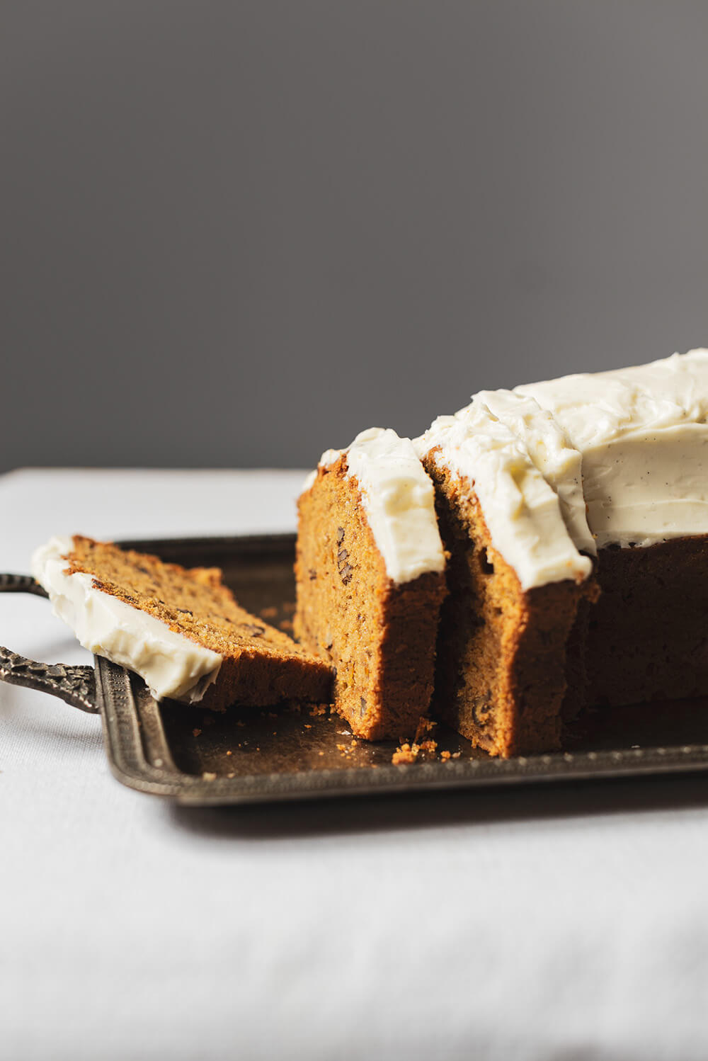 Bizcocho de zanahoria y nueces esponjoso fácil En una mesa hay una bandeja vintage. En esta bandeja vintage está el bizcocho de zanahoria y nueces ya cortado. Se ve muy cremoso el frosting de queso crema. El bizcocho está super esponjoso.