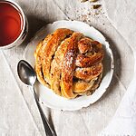 Bollos de cardamomo suecos esponjoso, recién horneado y espolvoreado con azúcar. Bollo trenzado junto a una taza de té caliente. Postre casero aromático y perfecto para acompañar el café o la merienda.