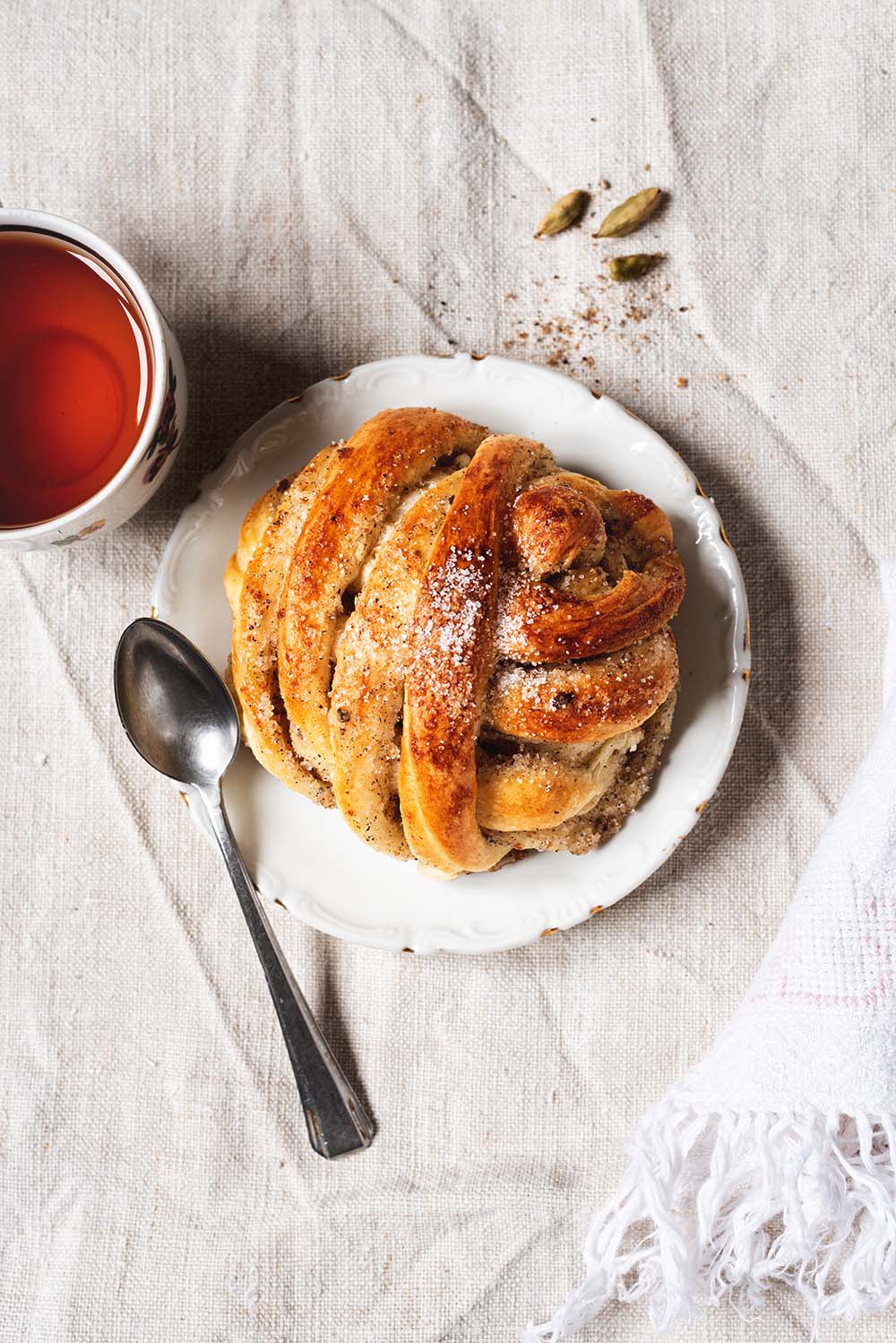 Bollos de cardamomo sueco esponjosos Bollos de cardamomo suecos esponjoso, recién horneado y espolvoreado con azúcar. Bollo trenzado junto a una taza de té caliente. Postre casero aromático y perfecto para acompañar el café o la merienda.
