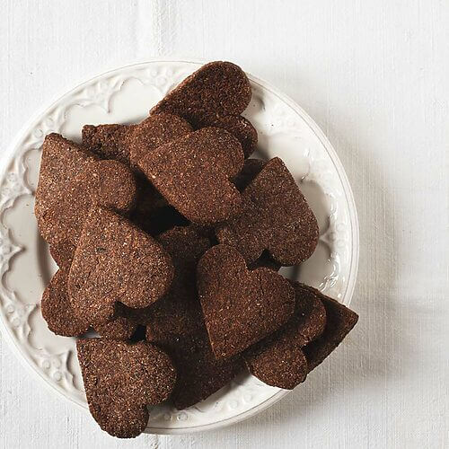 En una mesa hay un mantel blanco vintage. Encima hay un plato blanco lleno de Basler Brunsli.