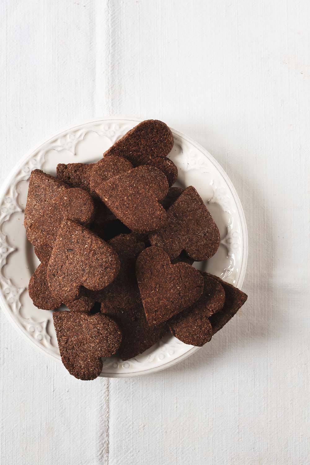 Galletas suizas de chocolate navideñas En una mesa hay un mantel blanco vintage. Encima hay un plato blanco lleno de Basler Brunsli.