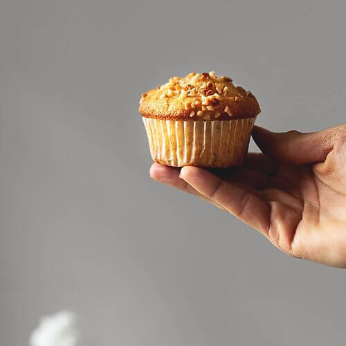Una mano está sujetando una magdalena de almendra que está decorada con almendras picadas. Se ve muy rica y dorada.
