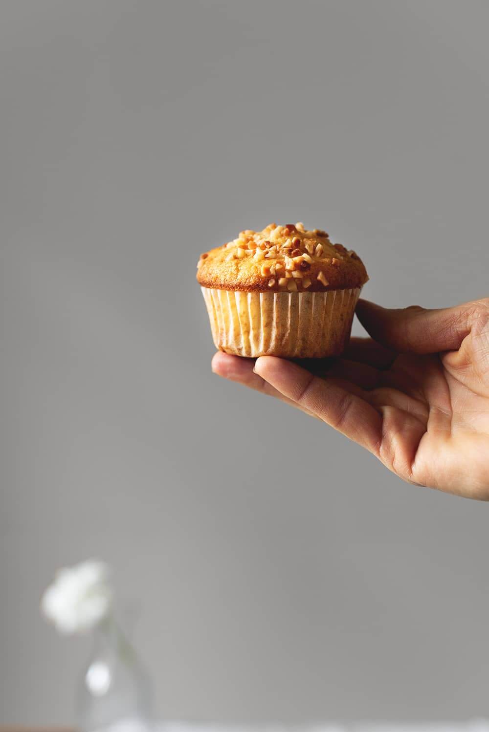 Una mano está sujetando una magdalena de almendra que está decorada con almendras picadas. Se ve muy rica y dorada.