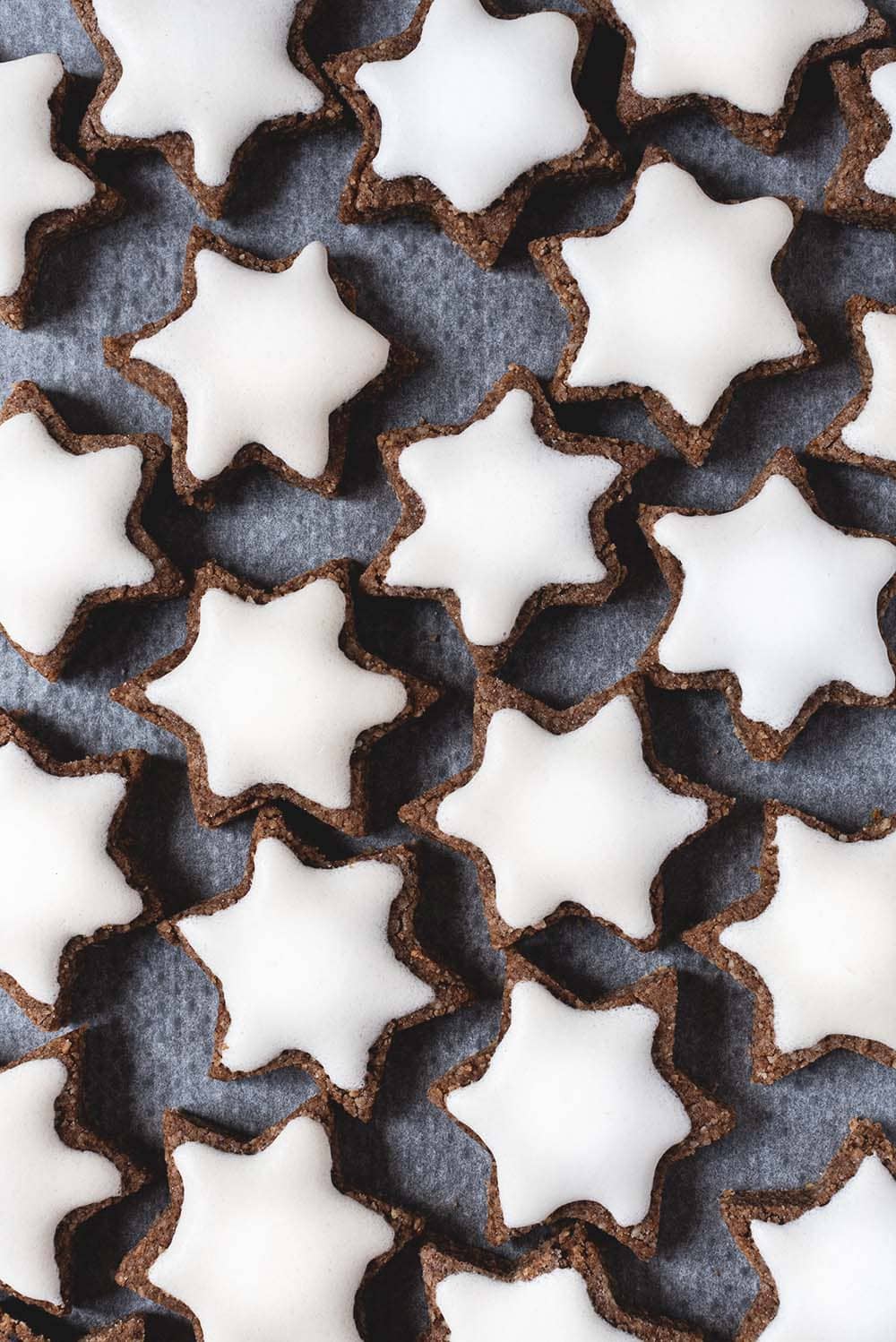 En una mesa hay papel de horno. En el papel están los Zimtsterne. Se ven muy bonitos su superficie blanca.