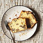 En un mantel gris hay un plato de color marrón claro. Encima hay dos rebanadas de bizcocho de nueces y yogur. En el plato hay un tenedor y migas