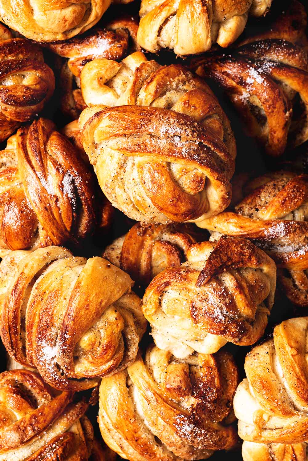 Receta de bollos de cardamomo sueco esponjosos Se ven muchos bollos de cardamomo recién hechos. Están dorados y tienen una pinta muy apetecible.