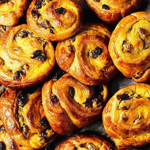 En un papel de cocina hay muchos Pains aux Raisins. Se ven doraditos jugosos y llenos de crema. Son muy apetecibles.