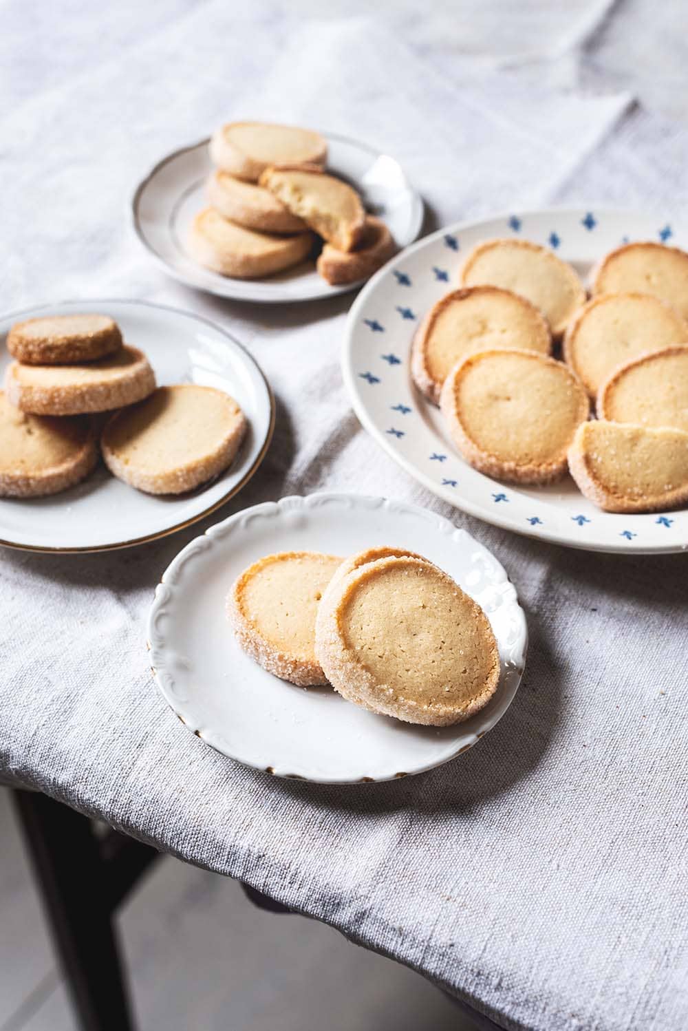 En una mesa de madera hay un mantel blanco. Encima hay cuatro platos llenos de Galletas Diamante. Se ven dorados en el contorno con su anillo de azúcar.