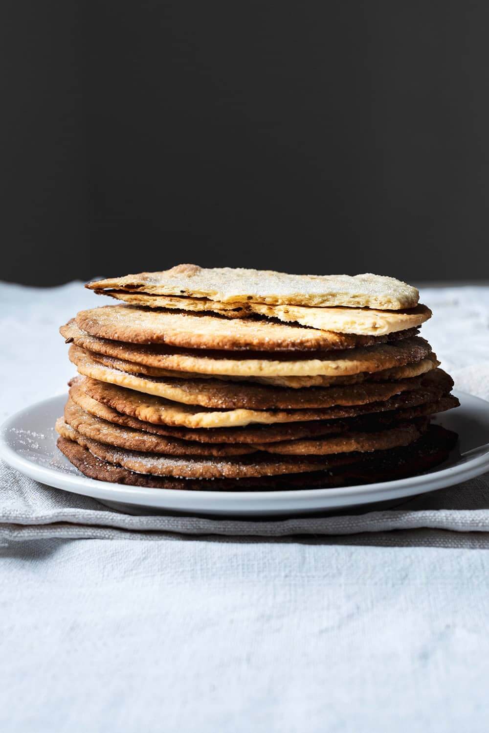 Cómo hacer tortas de aceite y anís En una mesa hay un mantel blanco. Encima hay varias tortas de aceite y anís puestas encima una y otra. La última está corta. Se ve tu textura crujiente.