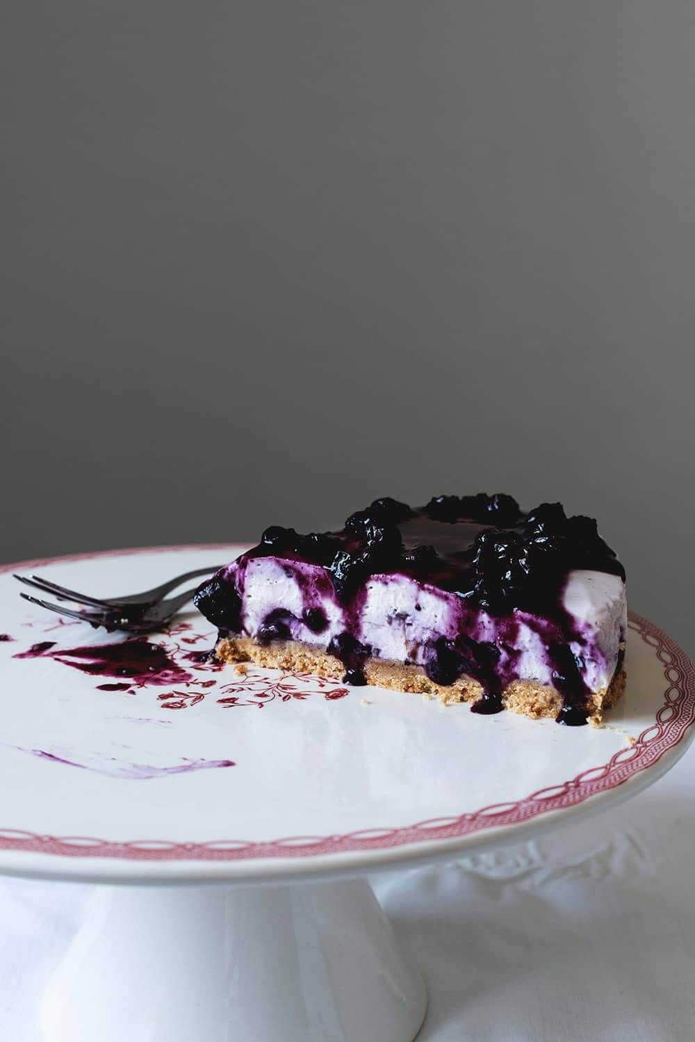 En una portatarta hay una ración de tarta de queso con arándanos sin horno. Se ve muy apetecible. Se ve muy rica la salsa de arándanos.