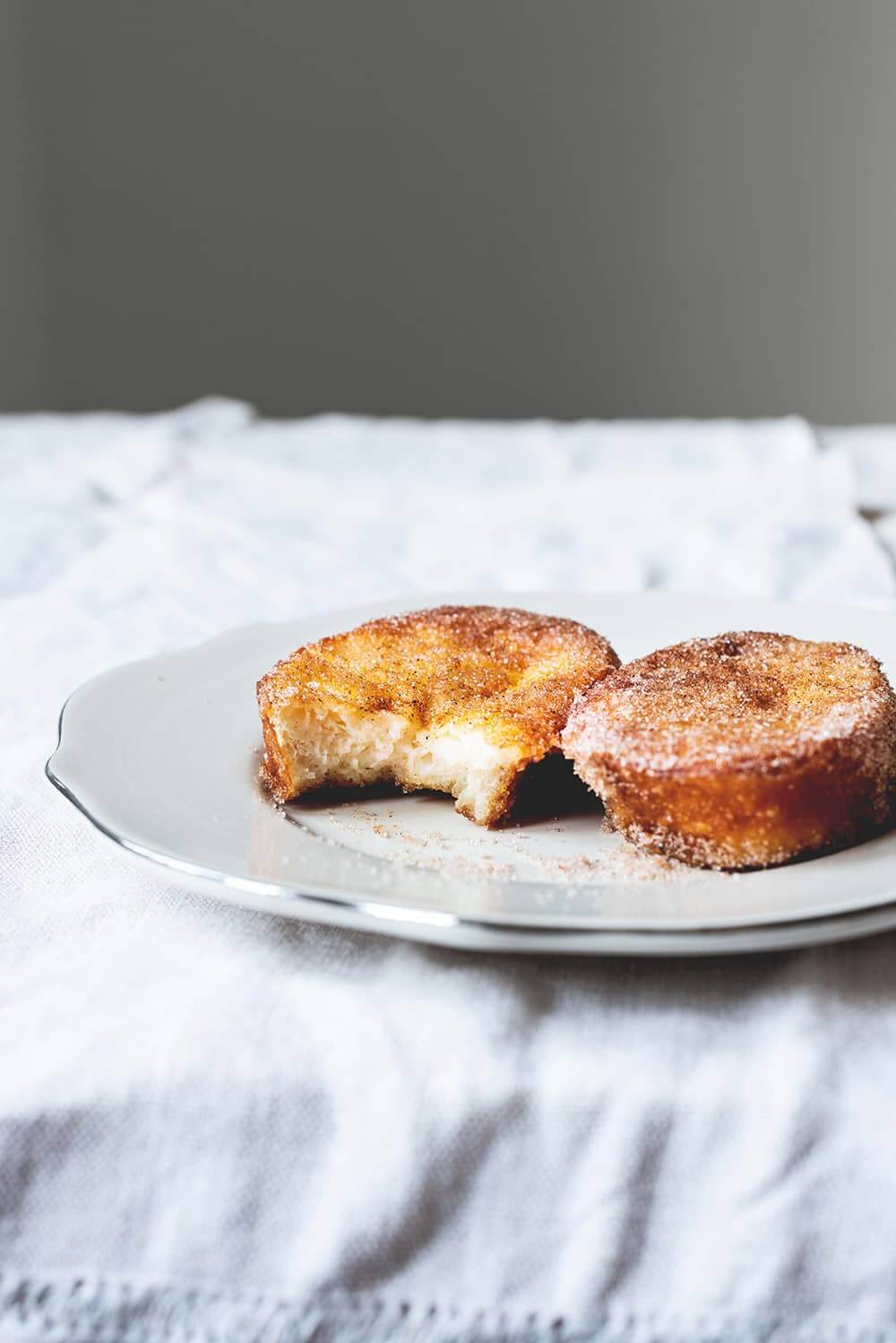 Receta de torrijas tradicionales Hay un mantel blanco en la mesa. Encima hay un plato blanco. Encima del plato hay dos torrijas de leche. Están doradas y apetitosas.