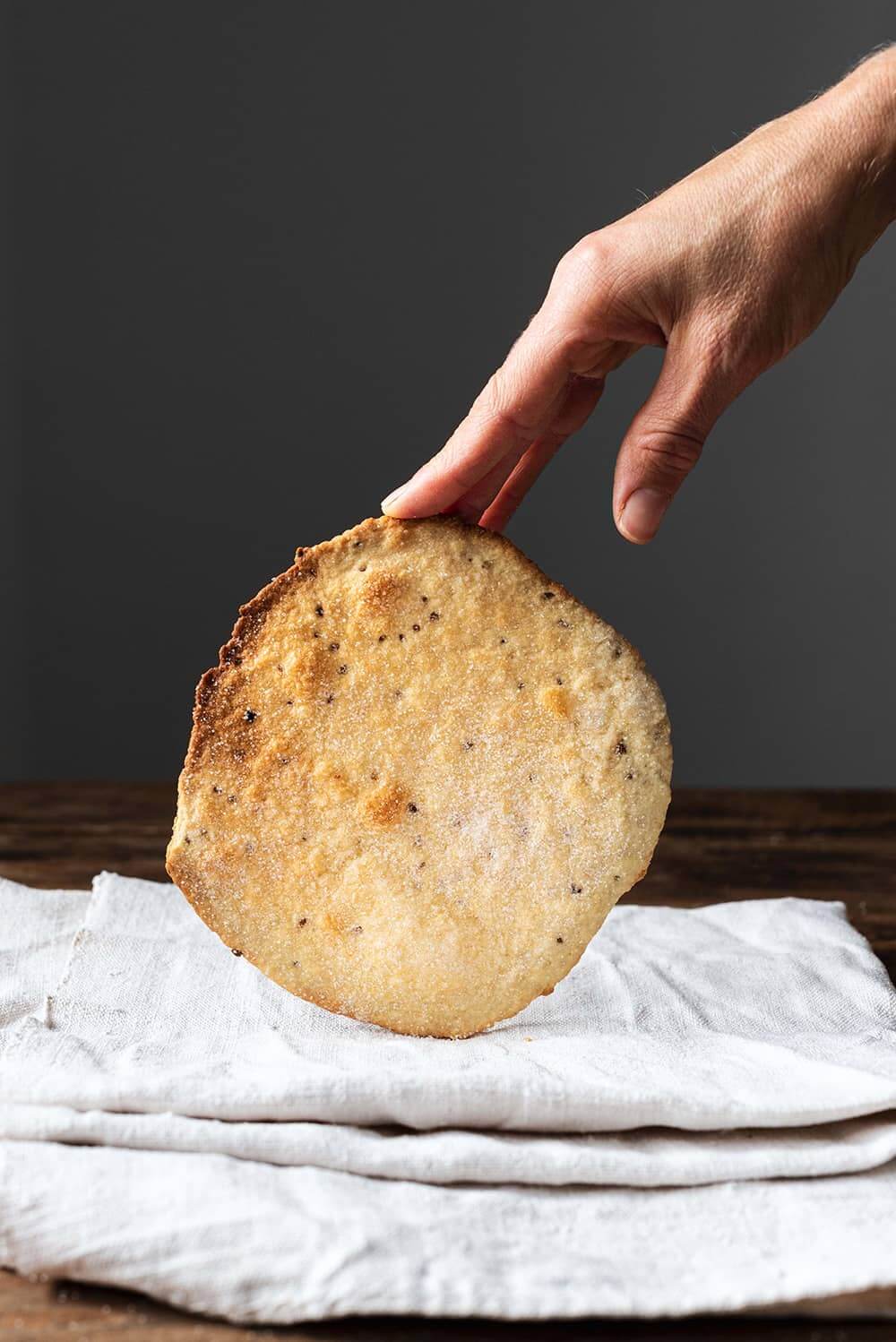 Tortas de aceite estilo Inés Rosales En una mesa de madera hay un paño blanco.Encima hay una torta de aceite estilo Inés Rosales . Unos dedos están sujetando esta torta.