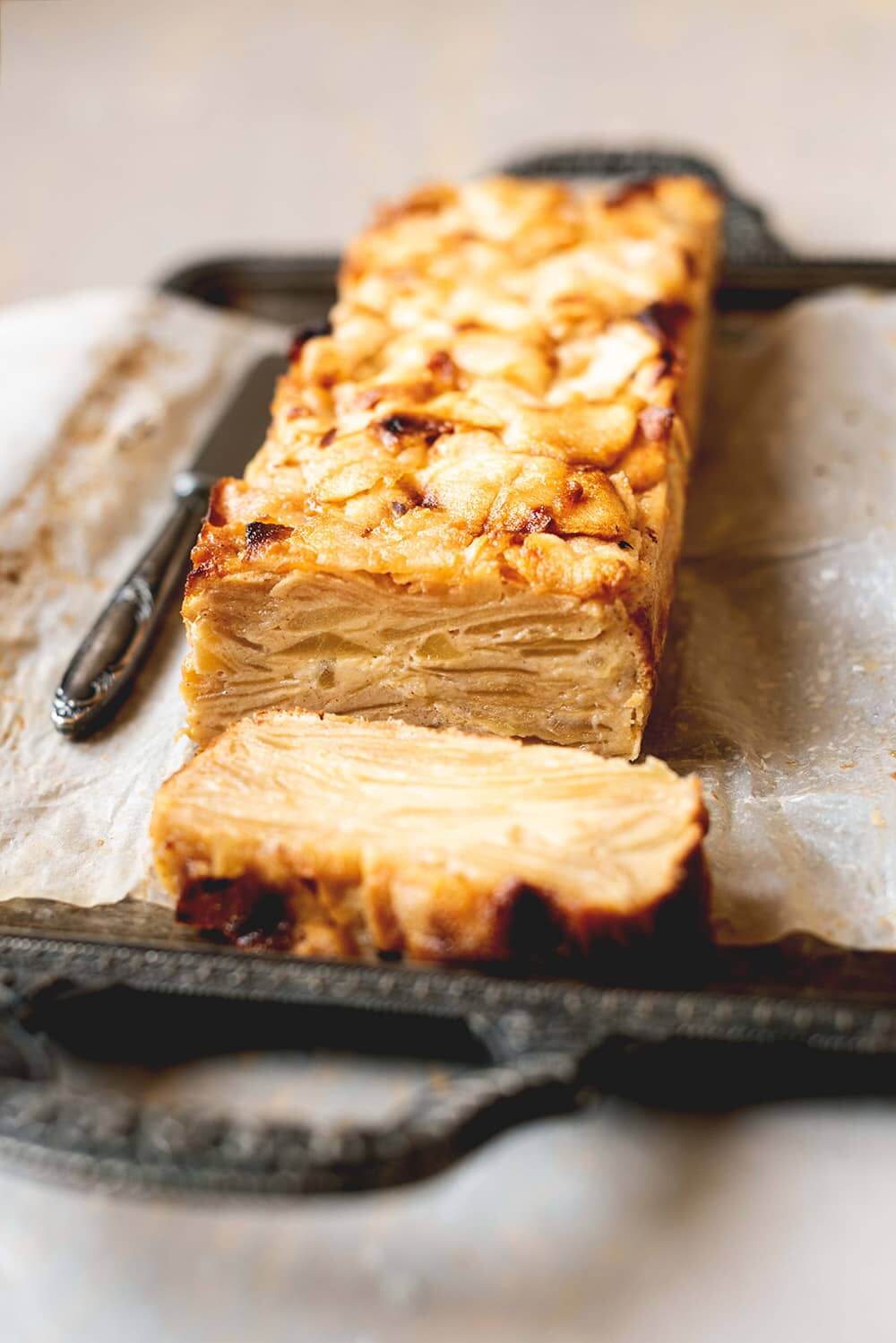 Receta de Pastel invisible de manzana En una bandeja vintage está en Pastel invisible de manzana. Está cortado y se ven las jugosas láminas de manzana.