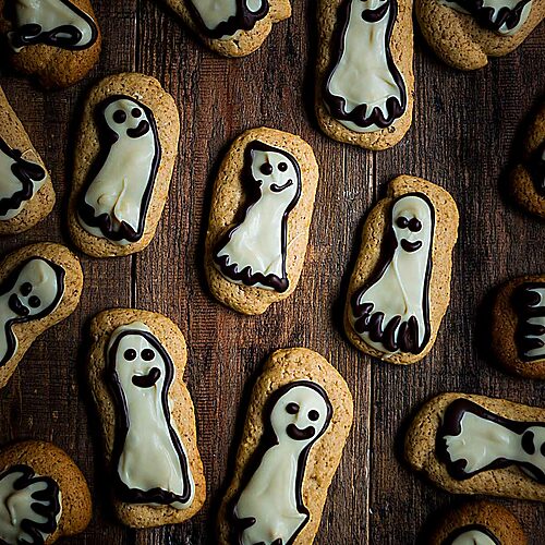 En una mesa de madera están las galletas de calabaza.Tienen una forma como fantasmas. Están decoradas con chocolate dando a cada una una carita bonita y agradable.